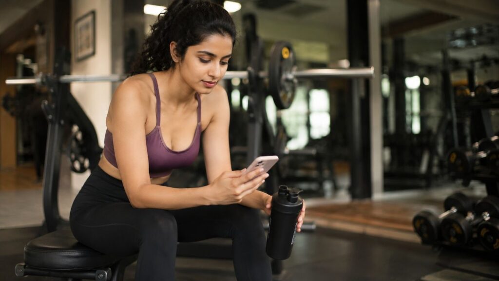 Woman researching pre-workout supplement questions on phone 
after gym workout session.